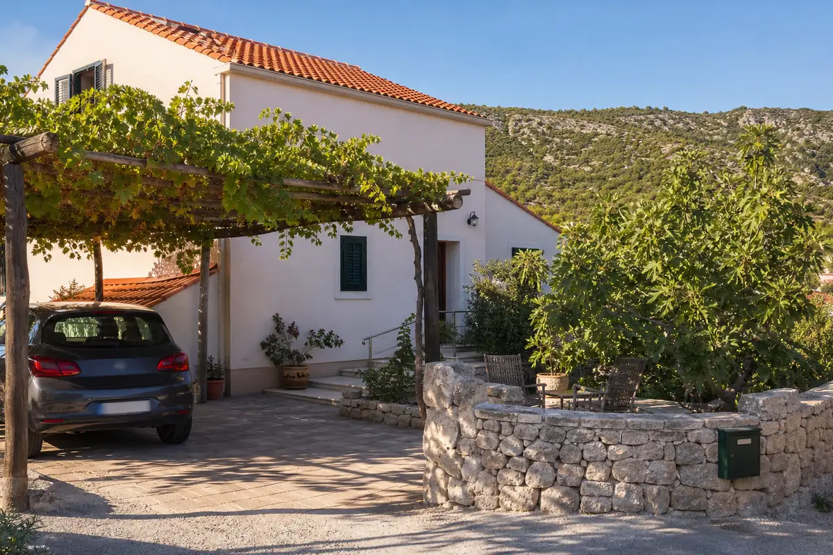 Eingangsseite eines kroatischen Ferienwohnungshauses mit Weinlaube über dem Stellplatz